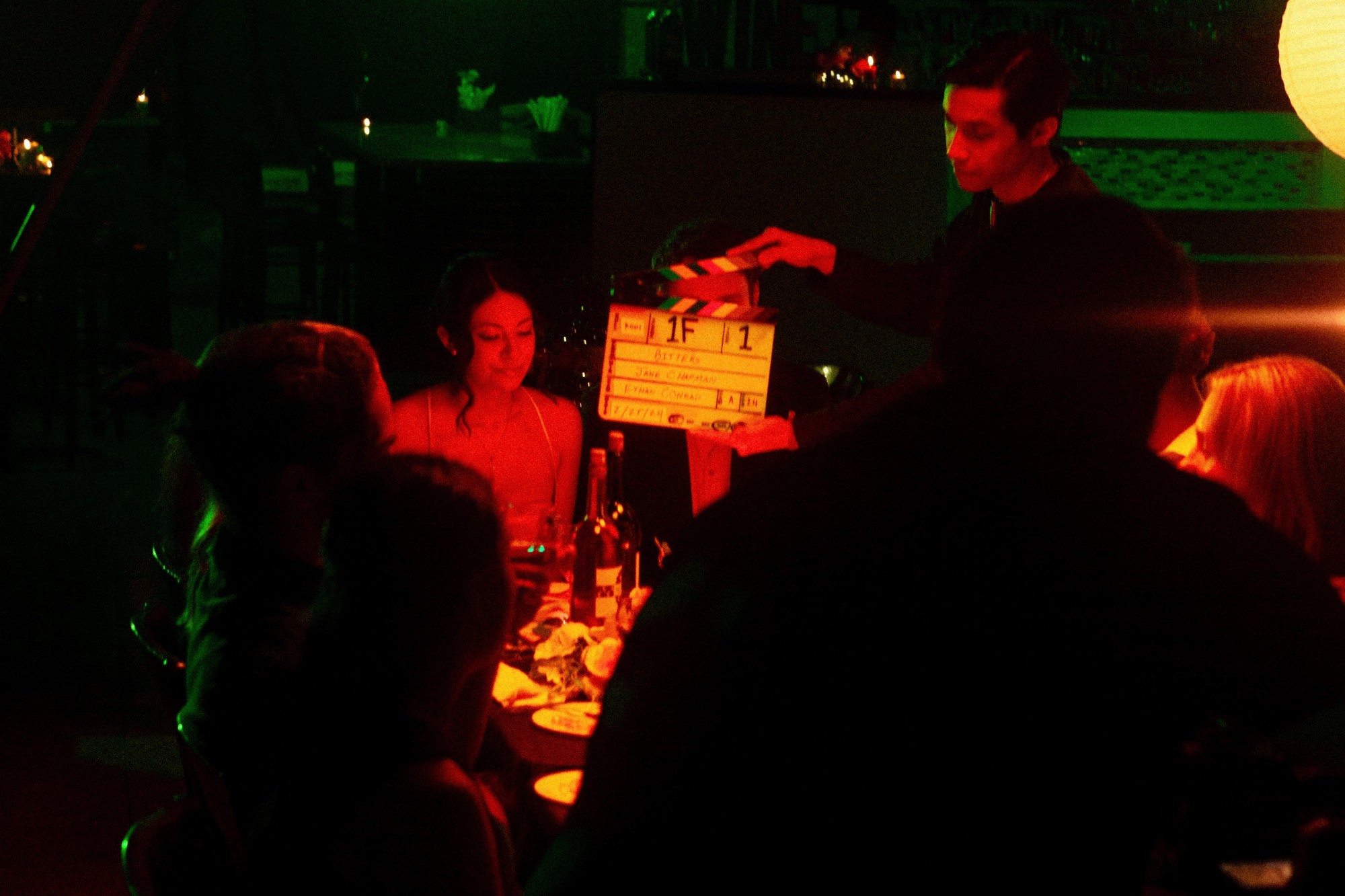 A film slate held over a candlelit dinner table on the set of Bitters